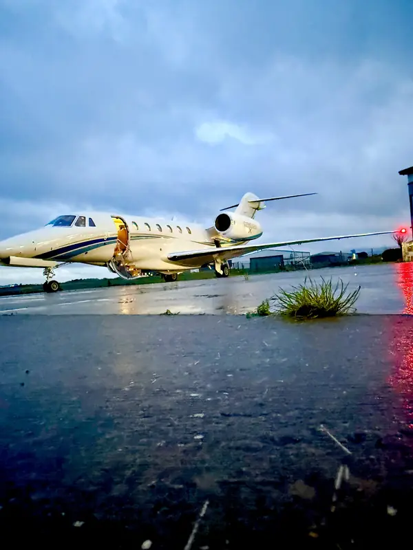 Citation X with the airstair door open and cabin lit, on a wet apron at dusk