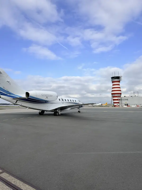 Cessna Citation X parked on the ramp under a blue sky, a red and white striped control tower behind